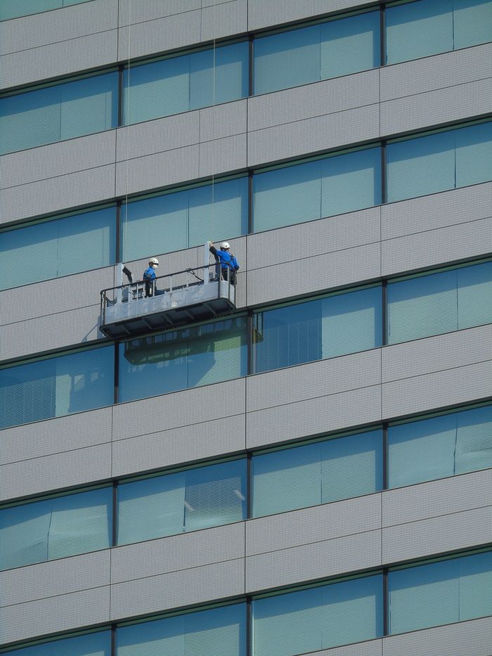 Two workers clean windows on a modern glass building facade using a suspended platform.
